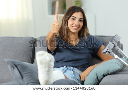Happy disabled woman with thumbs up sitting on a couch in the living room at home Royalty-Free Stock Photo #1144828160