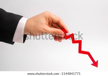 A businessman's hand is holding a red arrow down on a white background. The concept of reducing costs and profits, falling living standards and prices. Decreased projections, depressed economies.