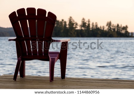 An empty chair sits at the end of a dock looking across a lake at dusk.