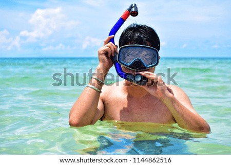 Portrait of a young asian man wearing swimming mask and snorkel on tropical beach with beautiful blue sky at Koh Samui, Thailand. Travel and Summer vacation swimming concept.