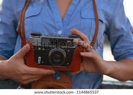 Beautiful hipster woman photographer in blue shirt holding vintage film camera in brown leather case