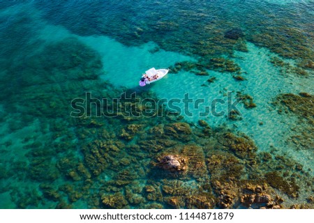 View from above, aerial picture of a rubber boat with some relaxed tourists on board is at anchor in the transparent and turquoise sea of the Emerald Coast (Costa Smeralda) in Sardinia, Italy.