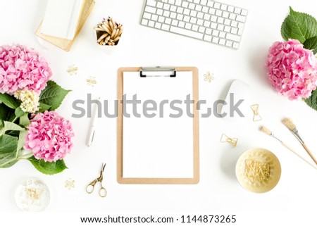 Stylized women's desk. Workspace with clipboard, computer, bouquet hydrangea, accessories on white background. Flat lay. Top view.
