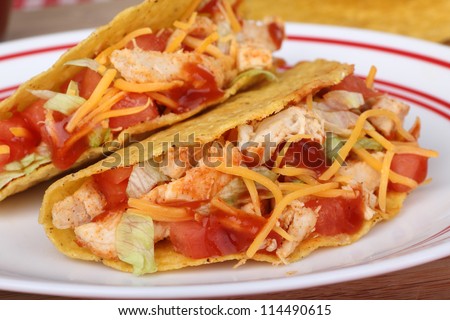 Closeup of two chicken tacos with tomato, lettuce, cheese and sauce on a plate