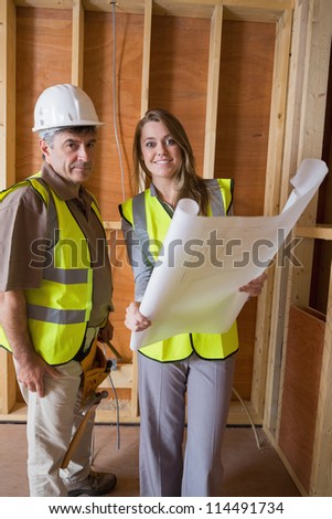 Smiling architects holding blueprints in construction site
