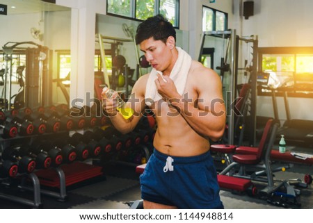 Asian man has muscle exercise in the gym.And Asian handsome muscles are tired, so drink Electrolyte drink.Exercise in gym concept.