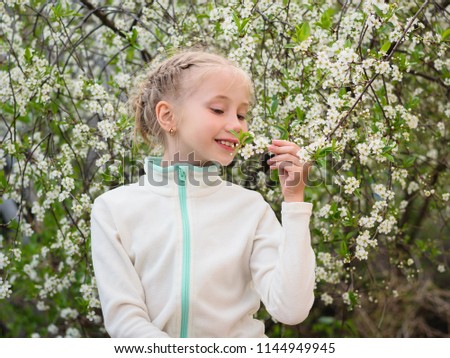 A beautiful girl in a sports jacket enjoys the aroma of cherry in the spring garden. Portrait of a girl on a background of cherry blossoms.