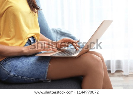 Young woman with modern laptop sitting on sofa at home, closeup