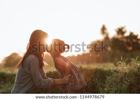 potrait of mother and daughter kissing and having fun in the field enjoying outdoor in beautiful sunset