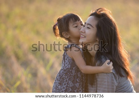 beautiful mom and kid kissing under the sunset sky in the meadow