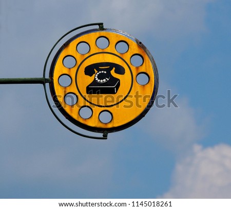 Old  rusty round  public telephone sign  with a black  rotary dial phone in the middle on yellow background.  Vintage italian signpost.
