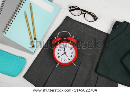 School uniform for girl and stationery on white wooden background, top view