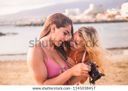 pretty couple of females models loooking together the summer pictures in the camera. smiles and fun. enjoy friendship and relationship in outdoor beach activiy