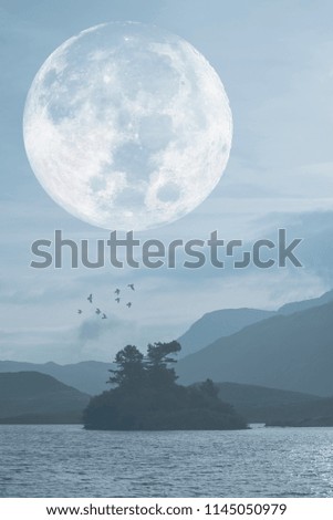 Misty landscape over still lake with mountain range and large super moon in background, elements of this image furnished by NASA