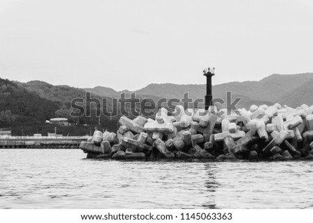Concrete dam and small lighthouse on sea with mountain background. Black and White picture