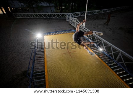 Back view of active man dressed in sporty clothes jumping on a trampoline on a summer evening