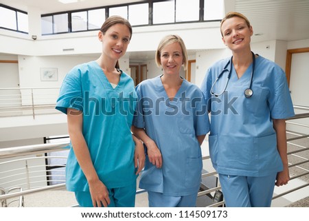 Three smiling nurses leaning against railing at hospital stairwell, Healthcare workers in the Coronavirus Covid19 pandemic