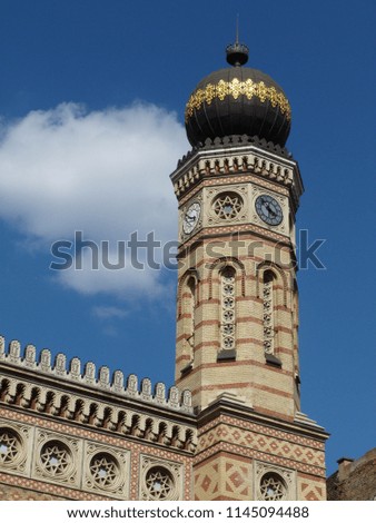 synagogue in Budapest with decorative  brick clock tower and facade under blue sky
