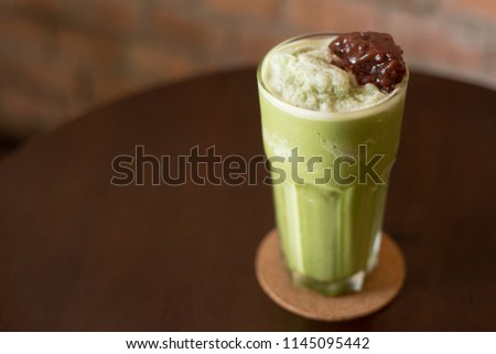 Green tea and sweet red bean topping on a wood table with brick wall background.