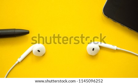 Blackpen and smartphone with earphone close up on yellow background
