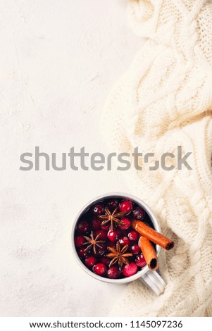 Mulled wine in cup with cranberry and spices on white sweater background