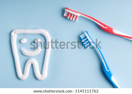 Toothpaste in a form of a smiling tooth. Red and blue toothbrushes. Toothpaste on blue. Dental hygiene. Royalty-Free Stock Photo #1145111762
