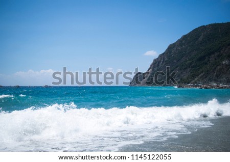 Awesome view of the sea with the white splashes that cover the sand. There is a mountain far away. Beautiful blue color of the water. Bright and colorful picture. 