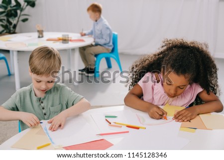 multicultural preschoolers drawing pictures with pencils in classroom
