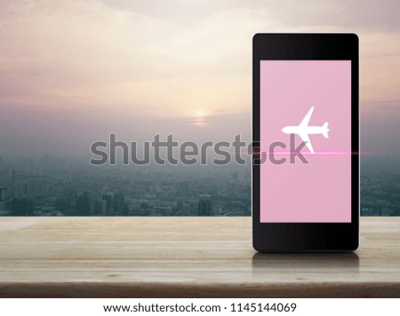 Airplane icon on modern smart phone screen on wooden table over city tower at sunset, vintage style, Business transportation concept