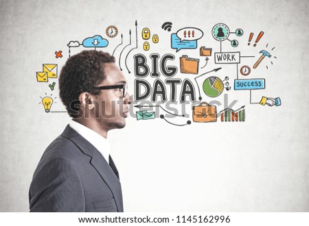 Side view of a young handsome African American businessman wearing glasses and a gray suit. A concrete wall background with a big data sktech on it.