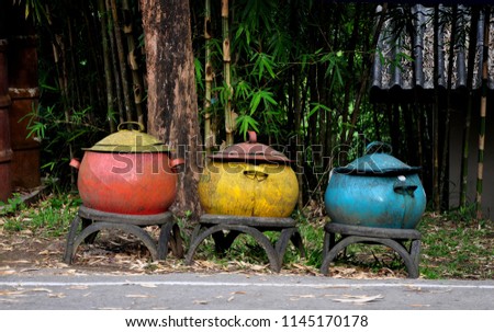 Colorful bins beside the road with bamboos, trees and the roof of the house background