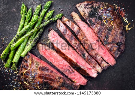 Barbecue dry aged wagyu flank steak sliced with green asparagus as top view on an old rusty board Royalty-Free Stock Photo #1145173880