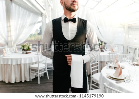 Waiter man in uniform holding a towel in his hand standing in a restaurant