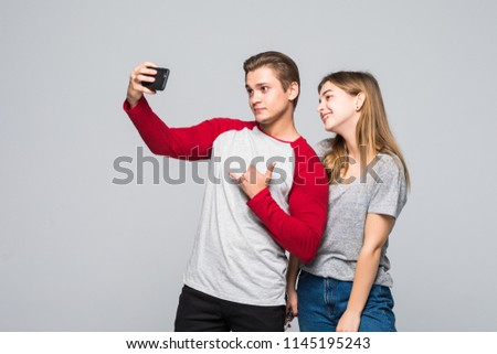 Portrait of a cheerful teenage couple taking selfie with mobile phone isolated