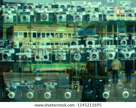 A blurred showcase of vintage cameras behind glass with a reflection of people and the urban landscape. Universal background. Nostalgia, photography, history. green color
