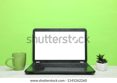 Laptop, a cup of tea and cactus on table on green background. Concept workplace.