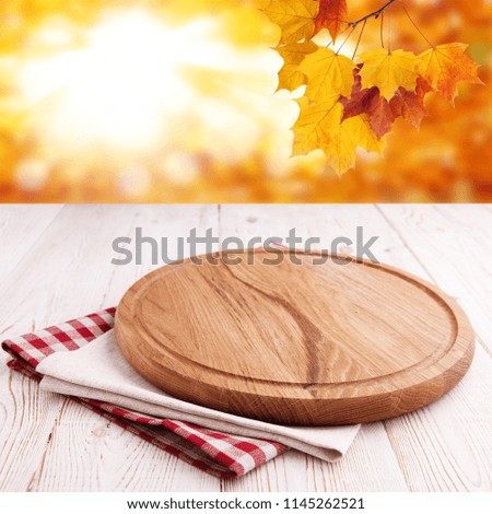 Pizza board and tableclothe on wooden desk. Autumn background. Top view mock up. Selective focus.