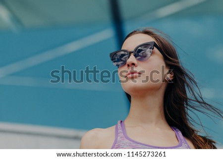 Horizontal shot of thoughtful male with dark hair, wears purple top and shades, feels self assured, likes healthy lifestyle, looks into distance, poses outdoor against blank copy space for promotion