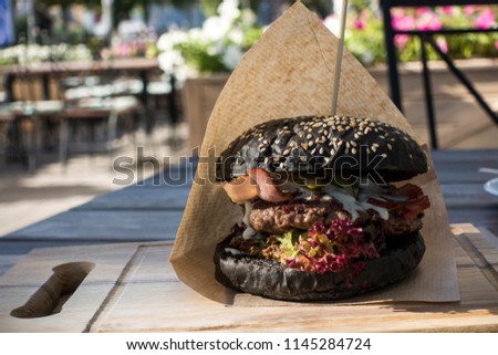 Fresh juicy tasty black burger with beef on wooden table in craft paper.