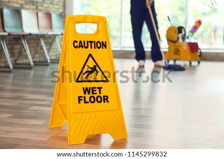 Safety sign with phrase Caution wet floor and blurred cleaner on background
