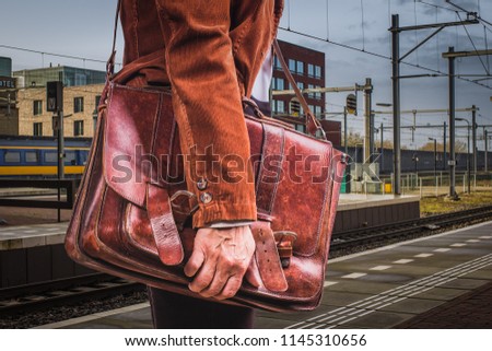 Train station, daily life. Hand of business men in corduroy jacket holds leather briefcase with documents, urban style, close-up Royalty-Free Stock Photo #1145310656