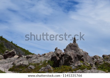 natural rock pile  topped with a  cairn pile, blue sky with light feather clouds in the background 
