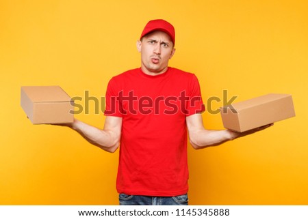Delivery man in red uniform isolated on yellow orange background. Professional male employee courier dealer in cap t-shirt holding empty cardboard boxes. Receiving package service concept. Copy space