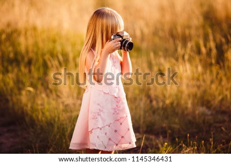 A little girl with a film camera takes pictures of nature in the summer
