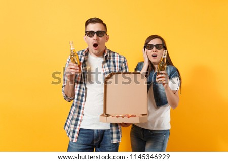 Young shocked couple woman man sport fan in 3d glasses cheer up support team hold beer bottles italian pizza in cardboard flatbox isolated on yellow background. Sport family leisure lifestyle concept