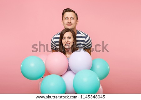Portrait of young fun crazy mad couple in love. Woman and man in blue clothes celebrating birthday holiday party on pastel pink background with colorful air balloons. People sincere emotions concept