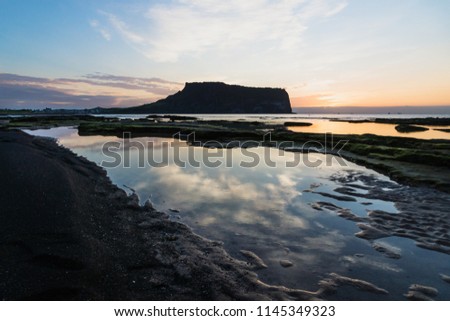 Cloud reflections in water at Sunrise at Ilchulbong volcano crater with view over ocean and green moss stones, Seongsan, Jeju Island, South Korea