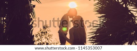 Silhouettes of mother and son, who meet the sunset in the tropics against the backdrop of palm trees BANNER, long format