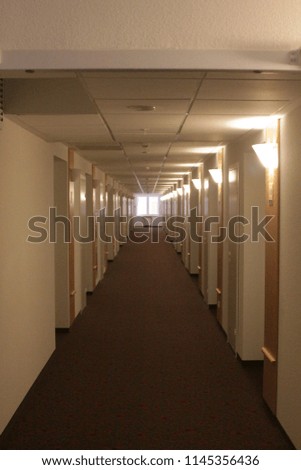 A long corridor with a bright window in the end of it and many lighten wall lamps on right and  not lighten on left and doors on both sides (vertical).