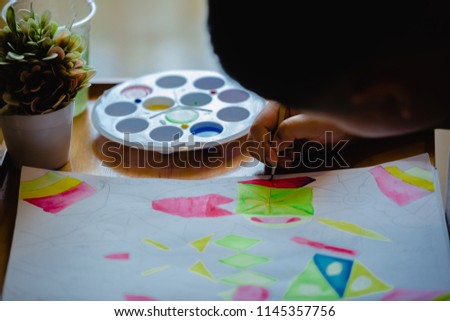 Concept of art, creativity and people. Hand of artist boy with brush painting picture. Painting With Watercolor Paints on a White Paper Book.
